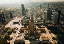 مشهد بانورامي لساحة مدينة وارسو القديمة يظهر المباني الملونة ذات الطراز الكلاسيكي والساحة العامة، يمثل نموذجاً عالمياً لإعادة الإعمار والحفاظ على الذاكرة المكانية