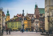 مشهد بانورامي لساحة مدينة وارسو القديمة يظهر المباني الملونة ذات الطراز الكلاسيكي والساحة العامة، يمثل نموذجاً عالمياً لإعادة الإعمار والحفاظ على الذاكرة المكانية