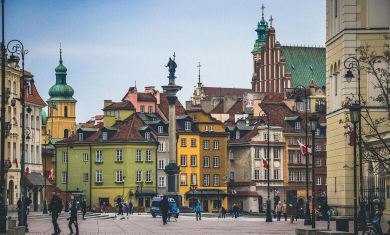 مشهد بانورامي لساحة مدينة وارسو القديمة يظهر المباني الملونة ذات الطراز الكلاسيكي والساحة العامة، يمثل نموذجاً عالمياً لإعادة الإعمار والحفاظ على الذاكرة المكانية