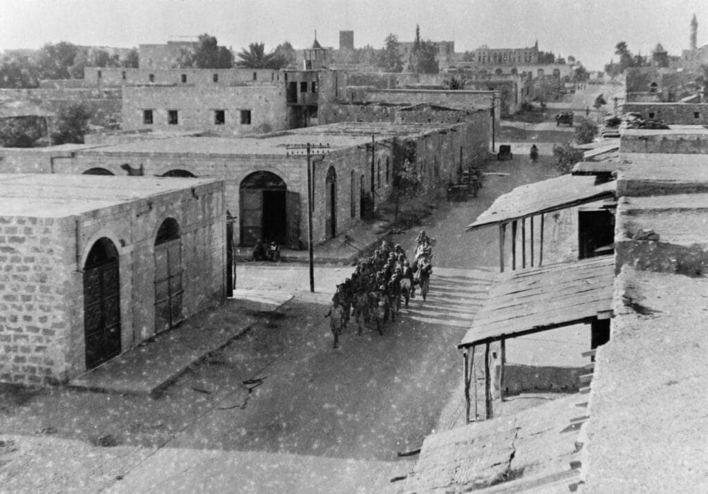 صورة تاريخية نادرة لمدينة غزة بالأبيض والأسود، تظهر العمارة التقليدية القديمة المبنية من الحجر، والأزقة الترابية الواسعة، وتعكس بساطة الحياة العمرانية في بدايات القرن الماضي.