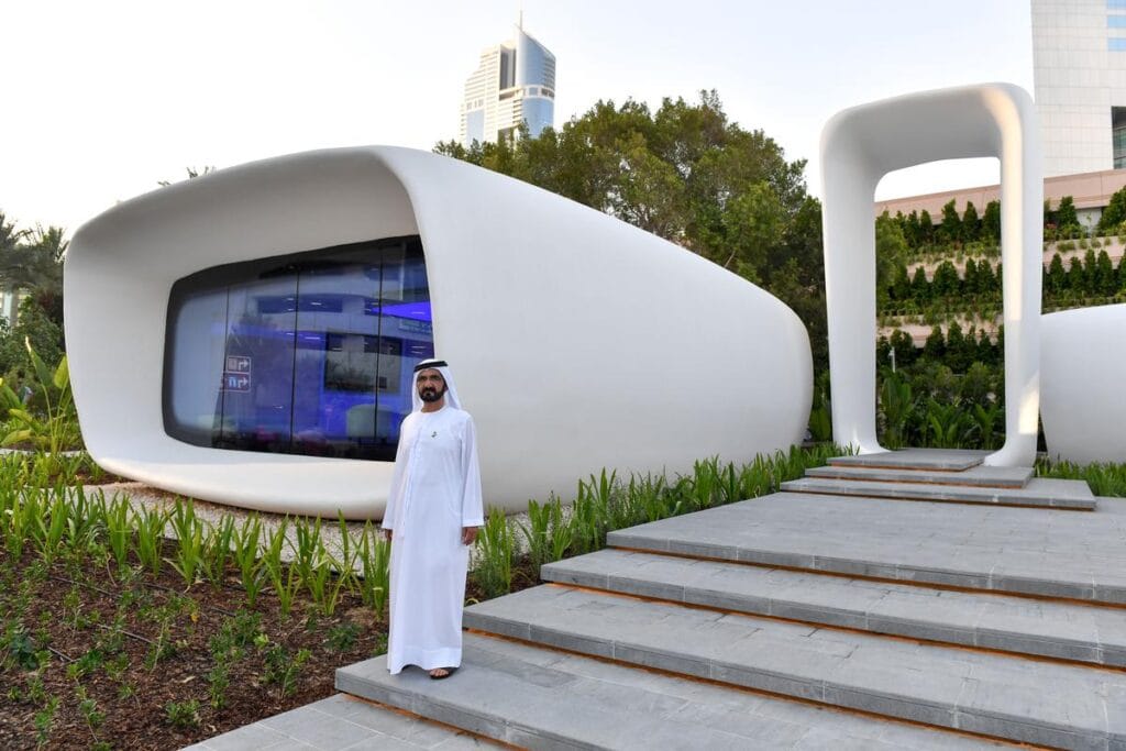 منظور خارجي لمبنى "Office of the Future" في دبي، أول مكتب إداري مطبوع بالكامل بـ تقنية الطباعة 3D من شركة Winsun، ويبرز التصميم الانسيابي المعاصر المتكامل مع المساحات الخضراء والسلالم الخارجية.