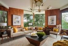 فراغ معيشة يجسد طراز Mid-Century Modern بكسوة جدران خشبية دافئة، أثاث بأرجل مدببة (Tapered Legs)، وثريا أيقونية، تطل على مساحات خضراء عبر نوافذ واسعة.