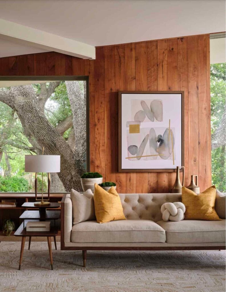 لقطة قريبة لفراغ معيشة بطراز Mid-Century Modern، تظهر أريكة أنيقة بأرجل خشبية نحيفة أمام جدار مكسو بالخشب الطبيعي، مع نافذة كبيرة تدمج الطبيعة الخارجية بالتصميم.