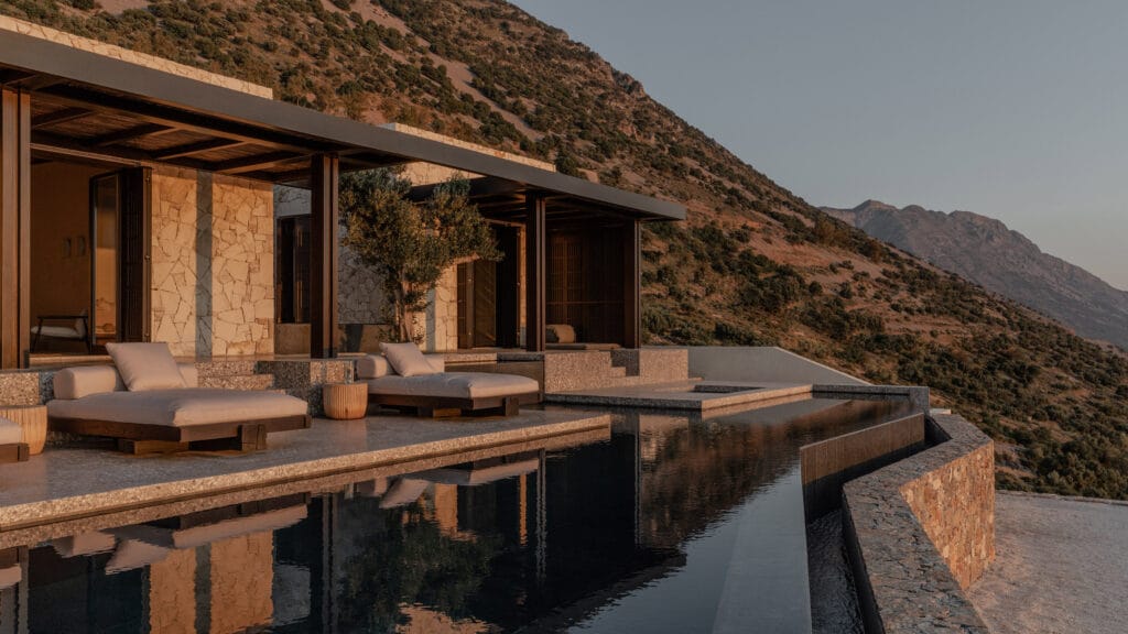 منظور معماري لمنزل 'Hill House' في جزيرة كريت، اليونان، يبرز تصميماً غاطساً جزئياً في التلة يتألف من كتل خرسانية أفقية متدرجة وشرفات واسعة تطل مباشرة على البحر، مع سقف أخضر يدمج الهيكل بالكامل في الطبيعة الجبلية المحيطة.