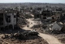 مشهد بانورامي لشارع مدمر في غزة، حيث تحول النسيج الحضري إلى تلال من ركام وأنقاض الرمادية التي تغلق الأفق العمراني.،