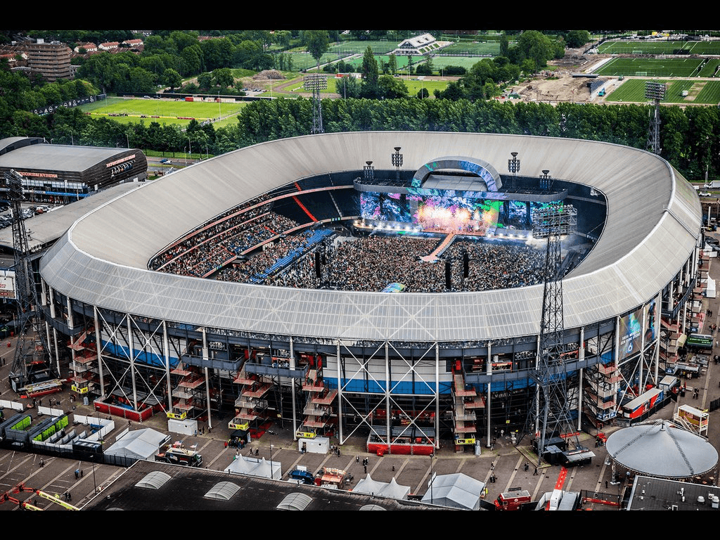 لقطة جوية لملعب دي كويب 'De Kuip' في روتردام، يظهر المدرجات المزدحمة وهيكل السقف الشفاف، كنموذج للملاعب الكلاسيكية التي حافظت على 'روح المكان' واندماجها الوظيفي في المدينة لعقود.