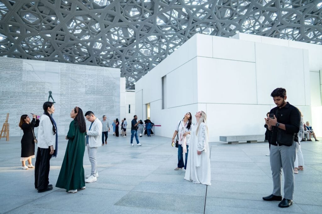 لقطة داخلية لمتحف اللوفر أبوظبي تظهر القبة الفراكتلية العملاقة التي تولد "مطر الضوء" الديناميكي، محاكيةً نفسياً وجسدياً ظلال سعف النخيل المريحة عصبياً.