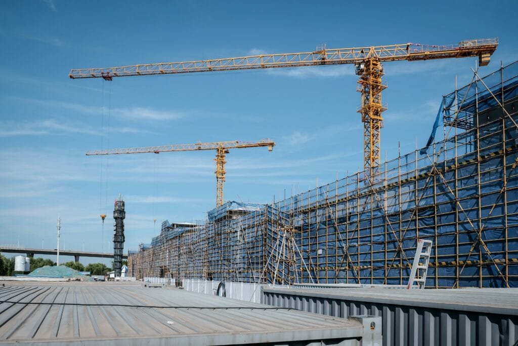 صورة لمشروع معماري ضخم Mega-Structures قيد الإنشاء تظهر فيها رافعات برجية صفراء ومجموعة واسعة من السقالات المعدنية المغطاة بشباك الحماية تحت سماء صافية